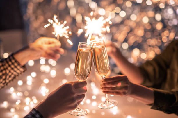 Hands of couple clinking with flutes of champagne and their friends holding sparkling bengal lights
